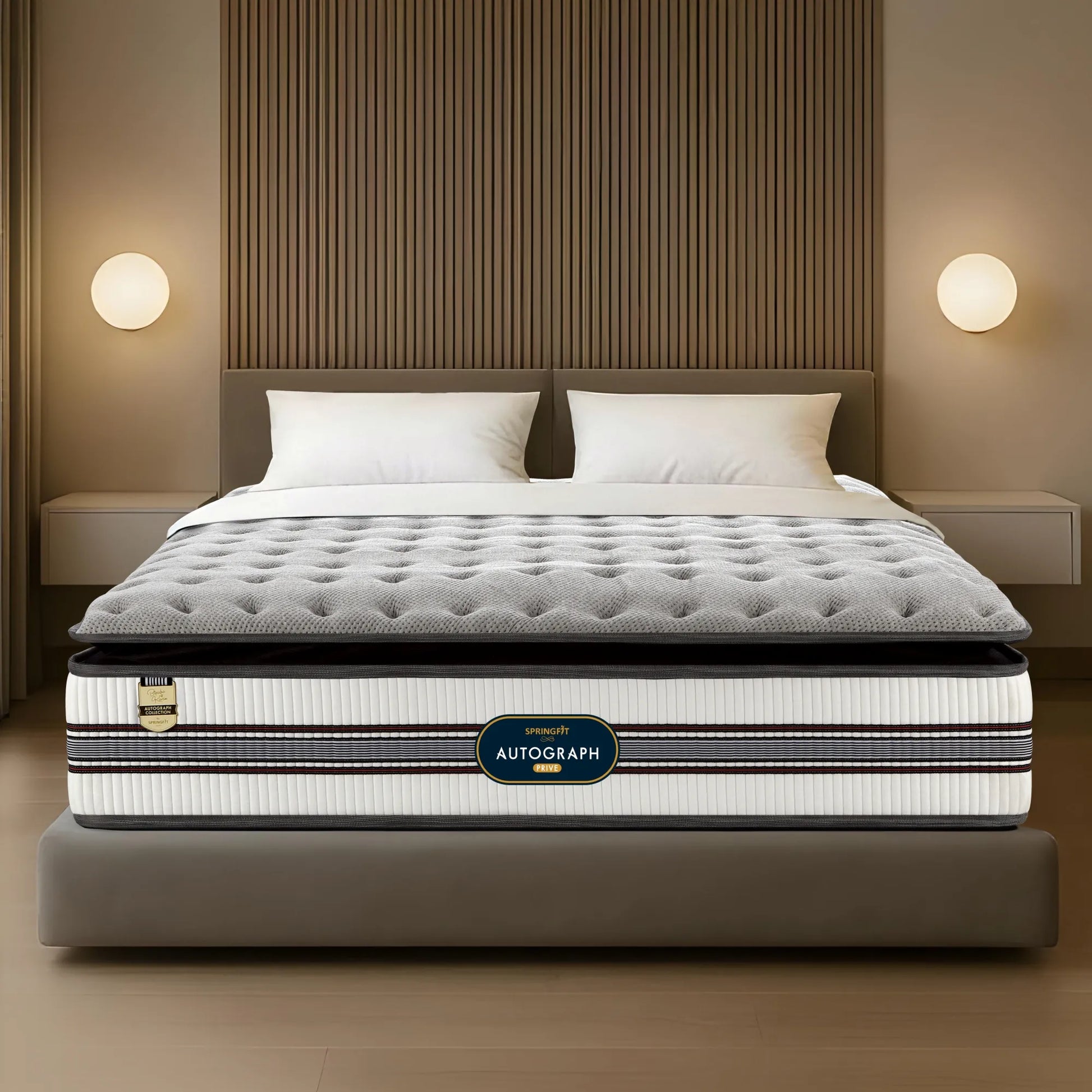 Front-facing view of the Springfit Autograph Prive mattress with a distinctive grey tufted pillow top and white striped border, displayed on a grey platform bed in a warm-lit bedroom with slatted wood wall panelling