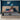 Springfit Betterspine Support mattress on a beige upholstered platform bed in a navy blue accent-wall bedroom, with a smiling couple in loungewear relaxing together — woman holding a drink and man browsing a laptop