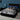 Springfit Betterspine Support mattress on a black platform bed with a tall dark channelled headboard in a navy blue bedroom, with a woman in grey activewear lying on her back in a relaxed sleeping position; teal table lamp and blue pillows visible