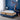 Springfit Club Class Natura luxury mattress lifestyle image with woman in navy blue dress seated on mattress edge on blue upholstered bed in navy blue accent bedroom with white lamp and abstract wall art