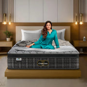 Springfit Club Class Petals luxury mattress lifestyle image with brand ambassador in teal outfit seated on grey scallop-quilted mattress on gold platform bed in elegant bedroom with gold pendant lights and wooden nightstands
