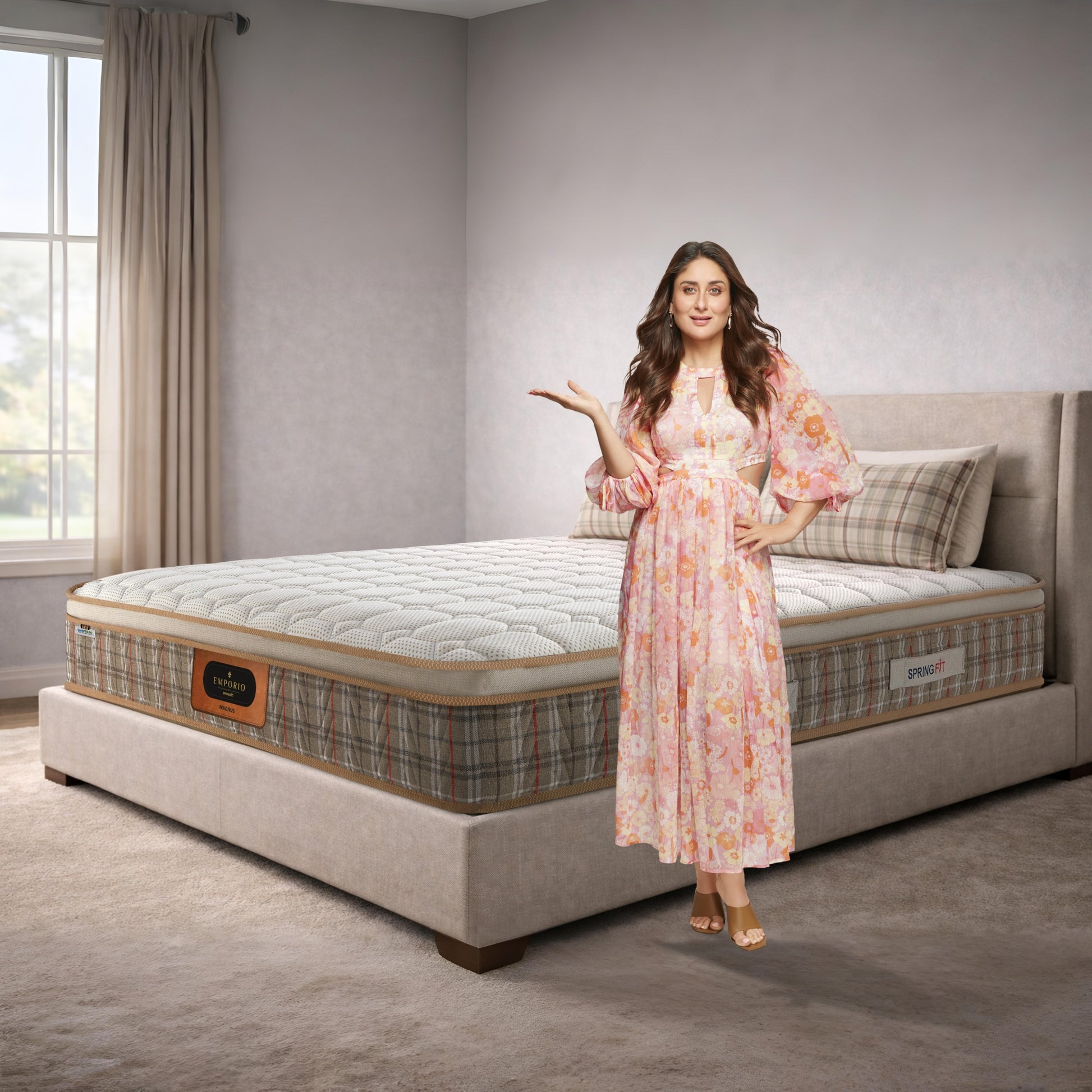 Springfit Emporio Magnus mattress on a beige upholstered bed in a light-toned bedroom with a brand ambassador in a floral dress presenting the product, featuring a distinctive tartan-patterned border and gold trim
