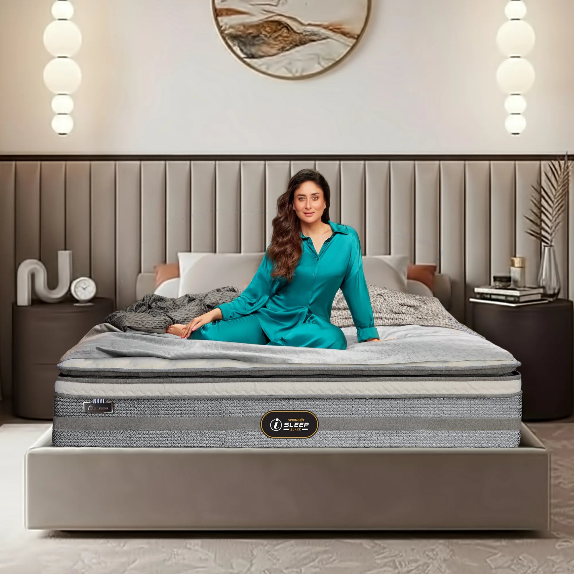 Springfit iSleep Black mattress on a beige upholstered bed with brand ambassador seated in a warm luxury bedroom with globe pendant lights