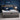 Springfit iSleep Blue mattress on a grey plaid upholstered wingback bed in a navy blue bedroom, with a man in blue loungewear working on a laptop while seated on the mattress
