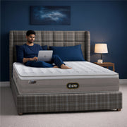 Springfit iSleep Blue mattress on a grey plaid upholstered wingback bed in a navy blue bedroom, with a man in blue loungewear working on a laptop while seated on the mattress