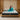 Springfit Premium Memory Foam mattress on a floating wooden platform bed in a warm wood-panelled bedroom with gold pendant lamps, with a brand ambassador in teal loungewear reclining casually on the mattress