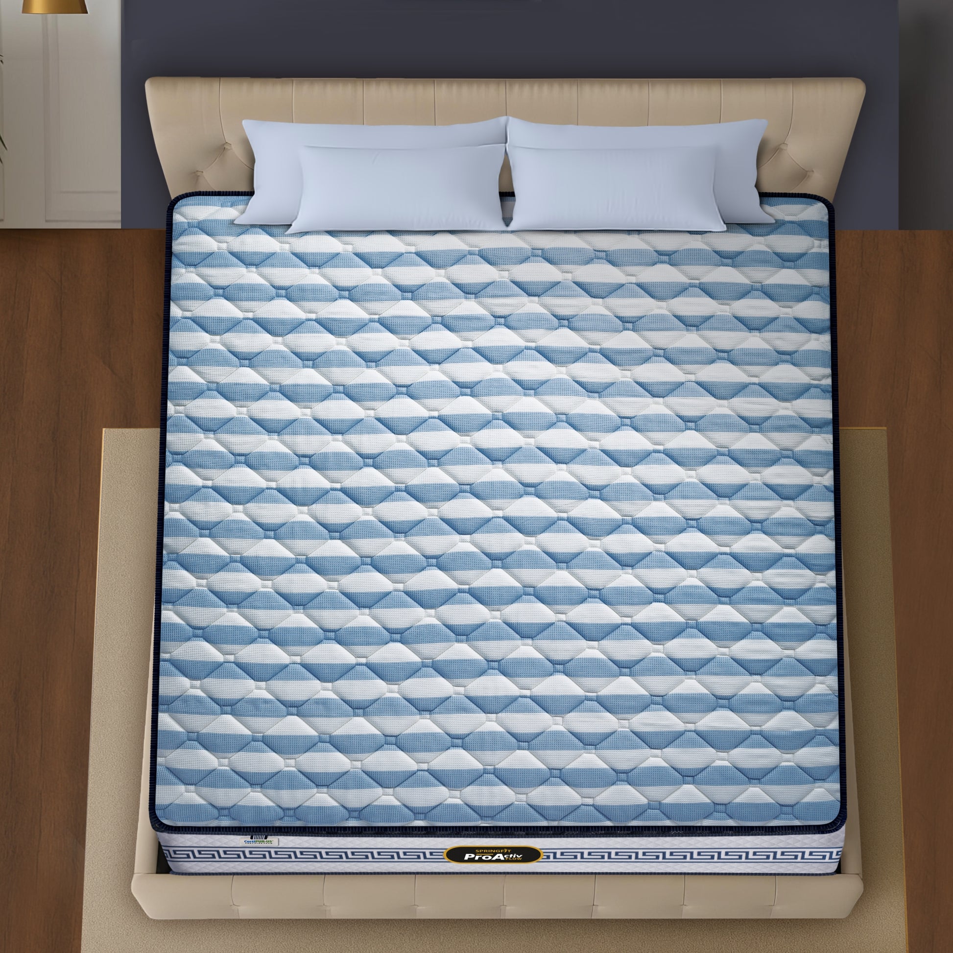 Springfit ProActiv Flow mattress aerial top view showing blue and white striped diamond-quilted surface on beige upholstered bed with light blue pillows in modern bedroom