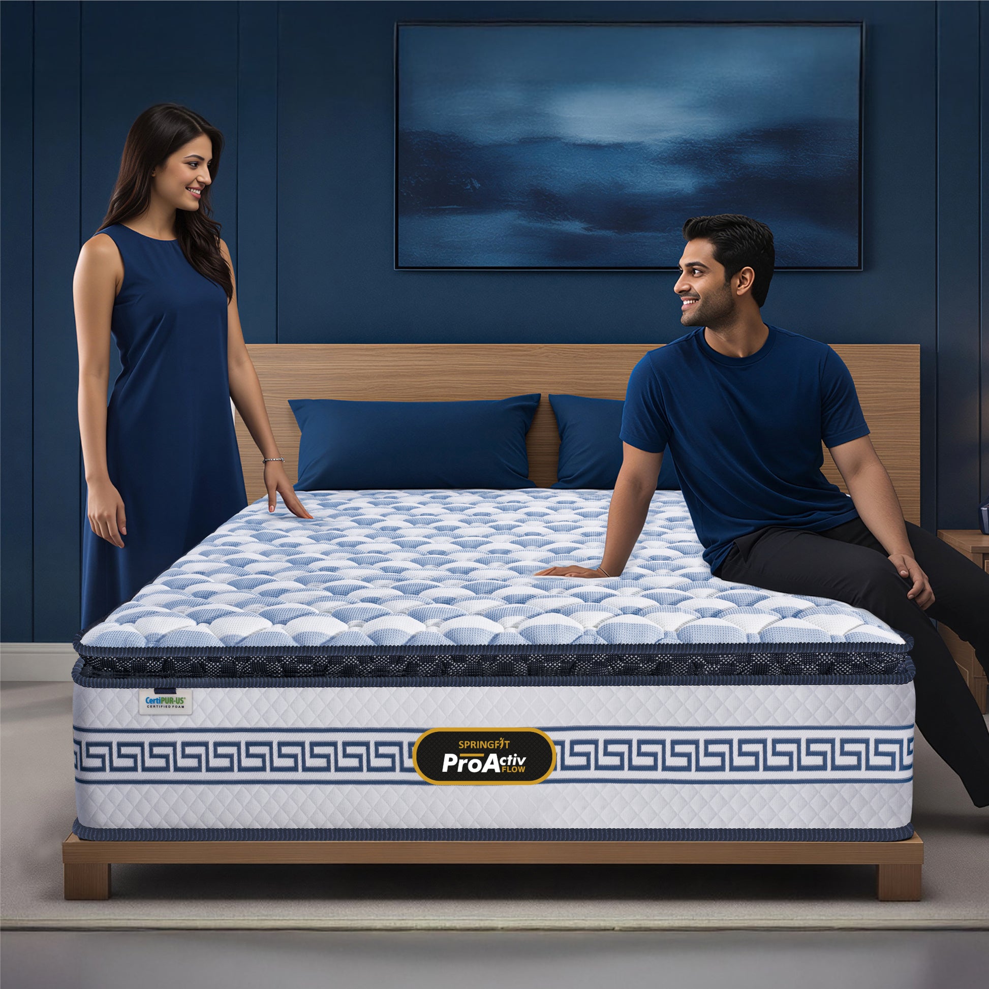 Springfit ProActiv Flow mattress with couple in navy blue outfits in deep blue accent bedroom with wooden headboard, blue cushions, and abstract wall art