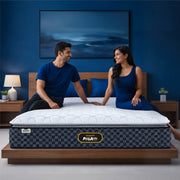 Springfit ProActiv Jump mattress with happy couple seated on king-size bed in blue accent bedroom with wooden headboard and matching nightstands