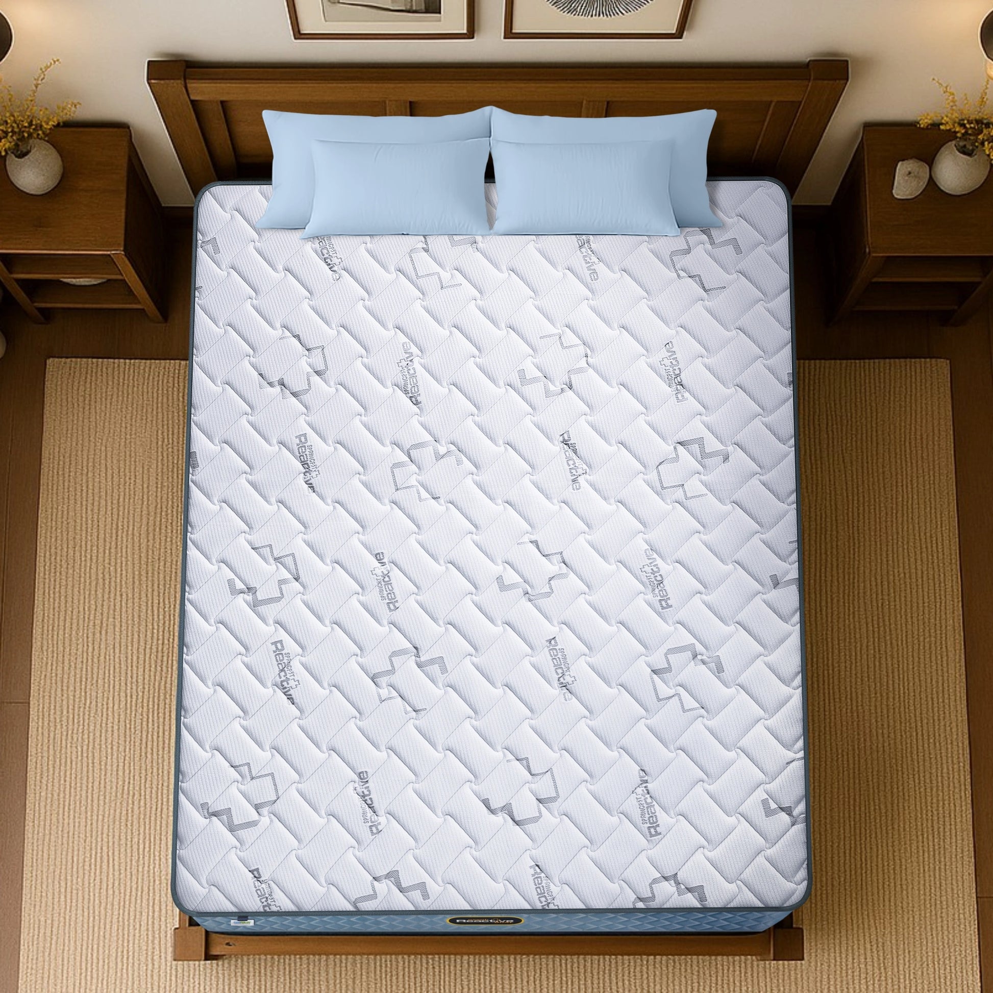 Springfit Reactive Dual mattress aerial top view showing white branded quilted fabric with logo pattern on wooden bed frame with light blue pillows and wooden nightstands