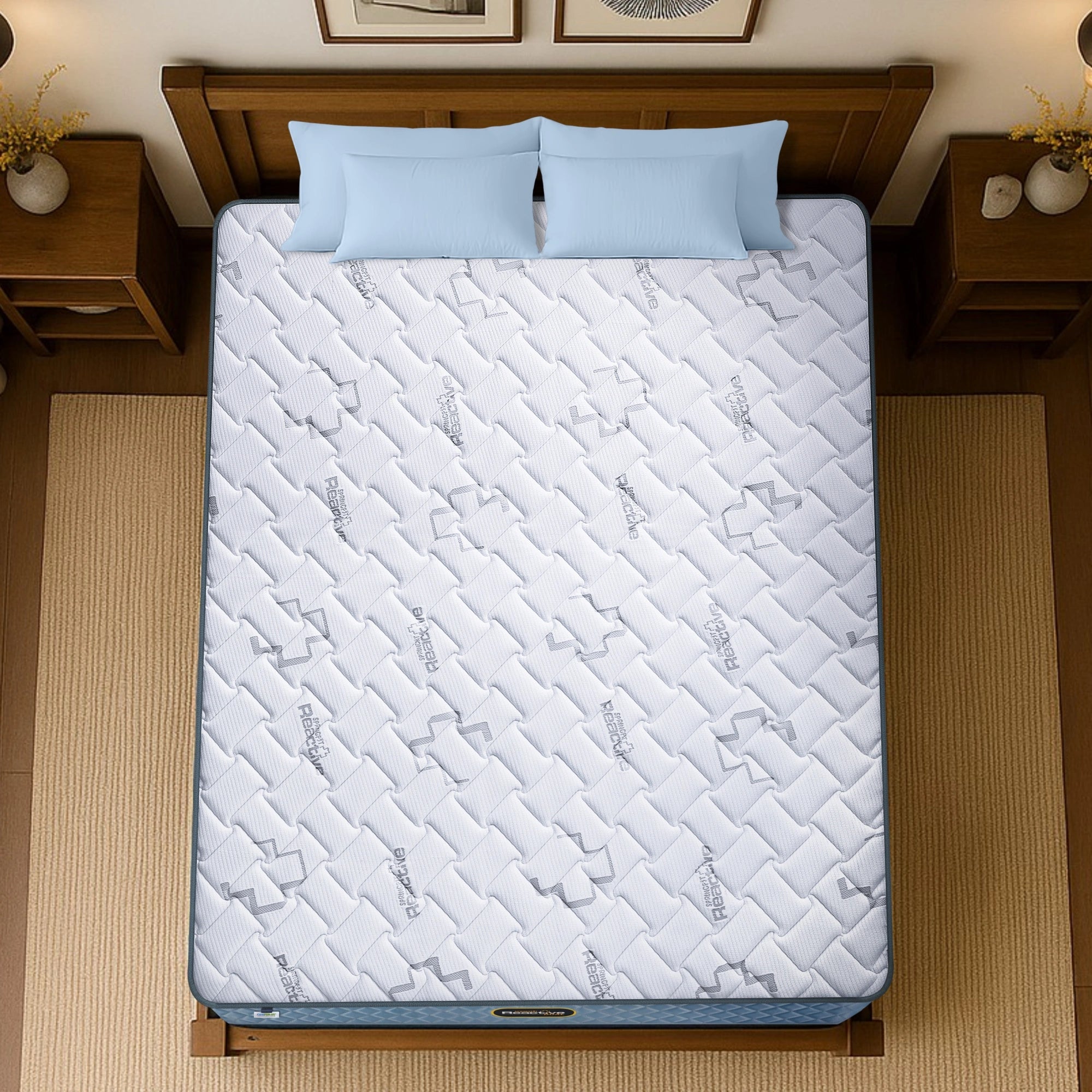 Springfit Reactive Dual mattress aerial top view showing white branded quilted fabric with logo pattern on wooden bed frame with light blue pillows and wooden nightstands
