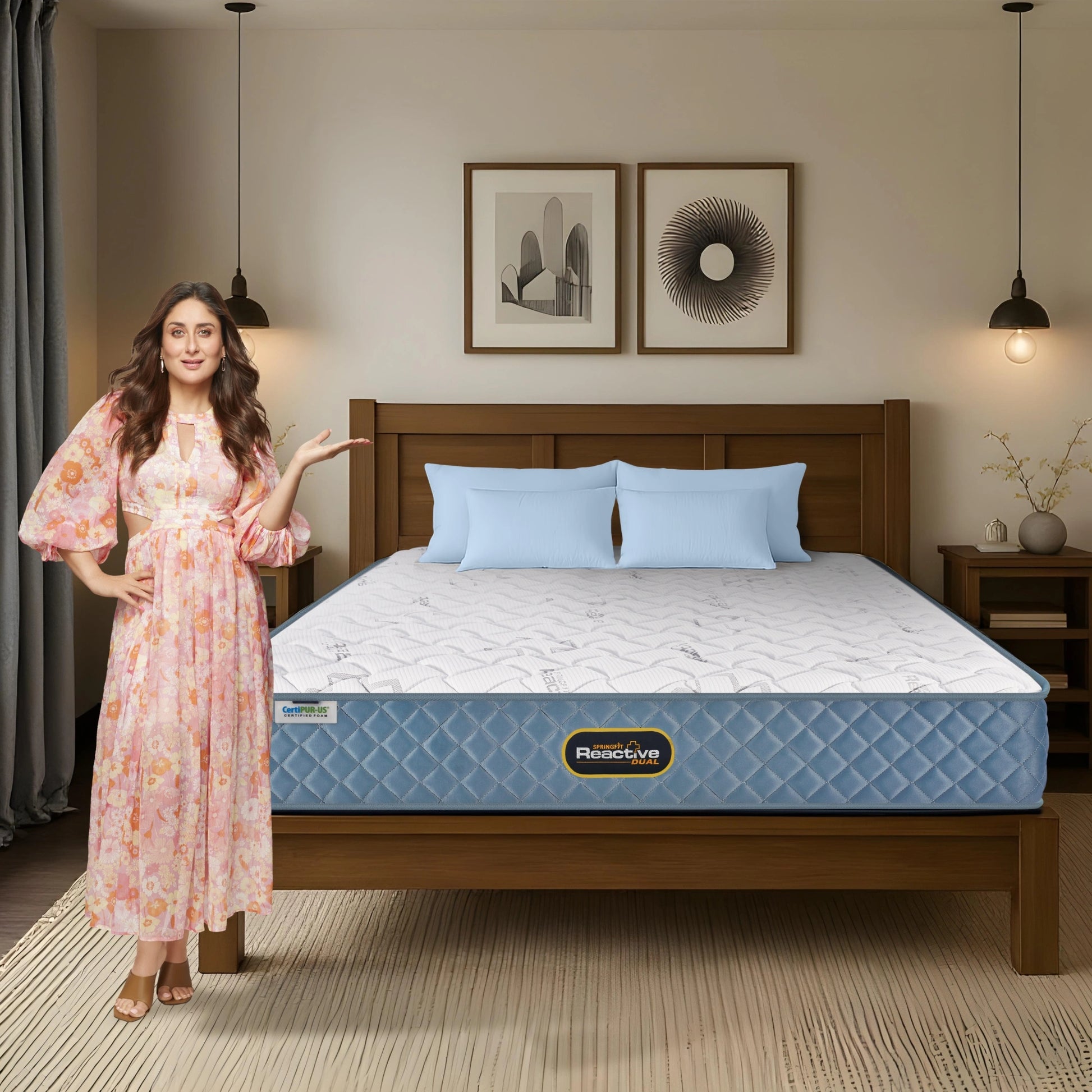 Springfit Reactive Dual mattress lifestyle image with brand ambassador in pink floral dress gesturing toward mattress on wooden bed with light blue pillows in warm neutral bedroom