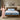 Springfit Reactive Dual mattress lifestyle image with brand ambassador in pink floral dress gesturing toward mattress on wooden bed with light blue pillows in warm neutral bedroom