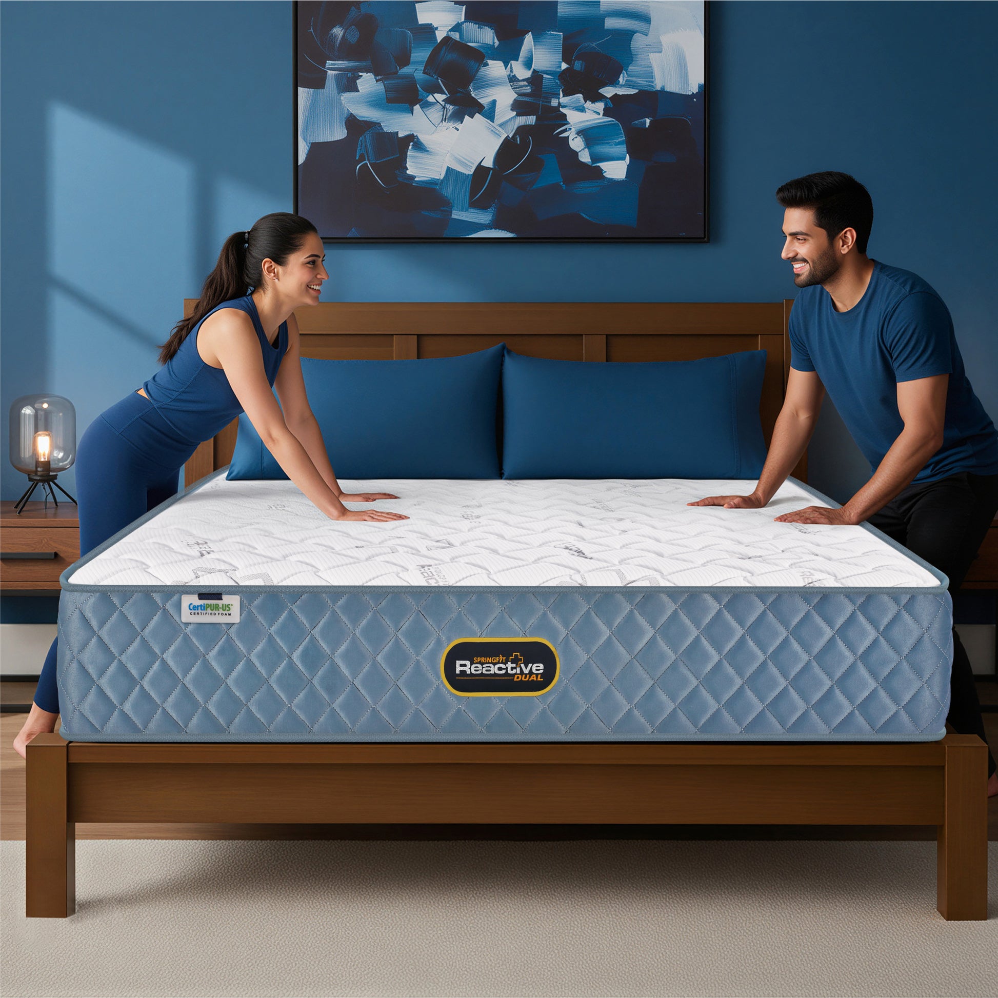 Springfit Reactive Dual mattress with smiling couple in matching navy outfits pressing the mattress surface on wooden bed frame in blue accent bedroom with abstract wall art