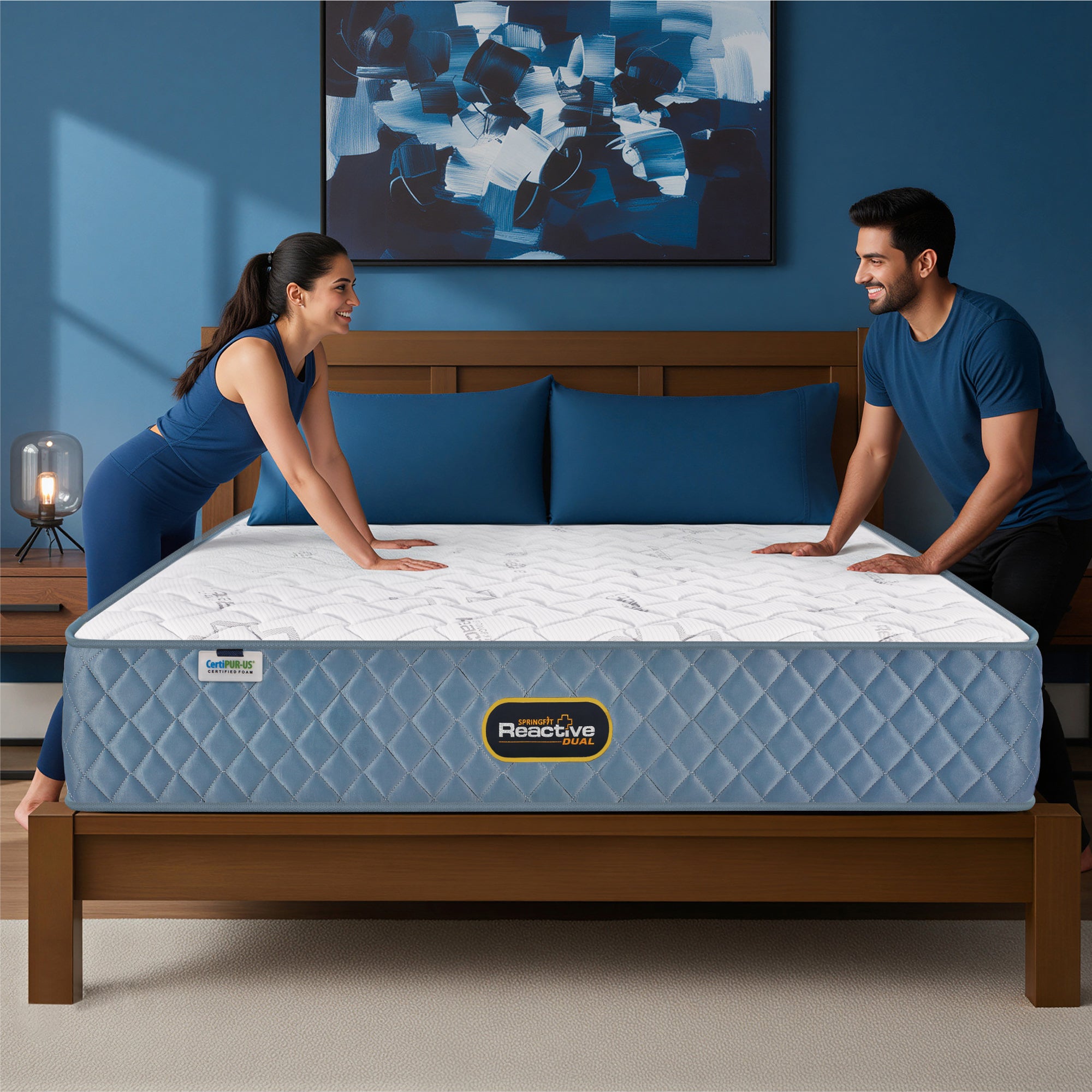 Springfit Reactive Dual mattress with smiling couple in matching navy outfits pressing the mattress surface on wooden bed frame in blue accent bedroom with abstract wall art