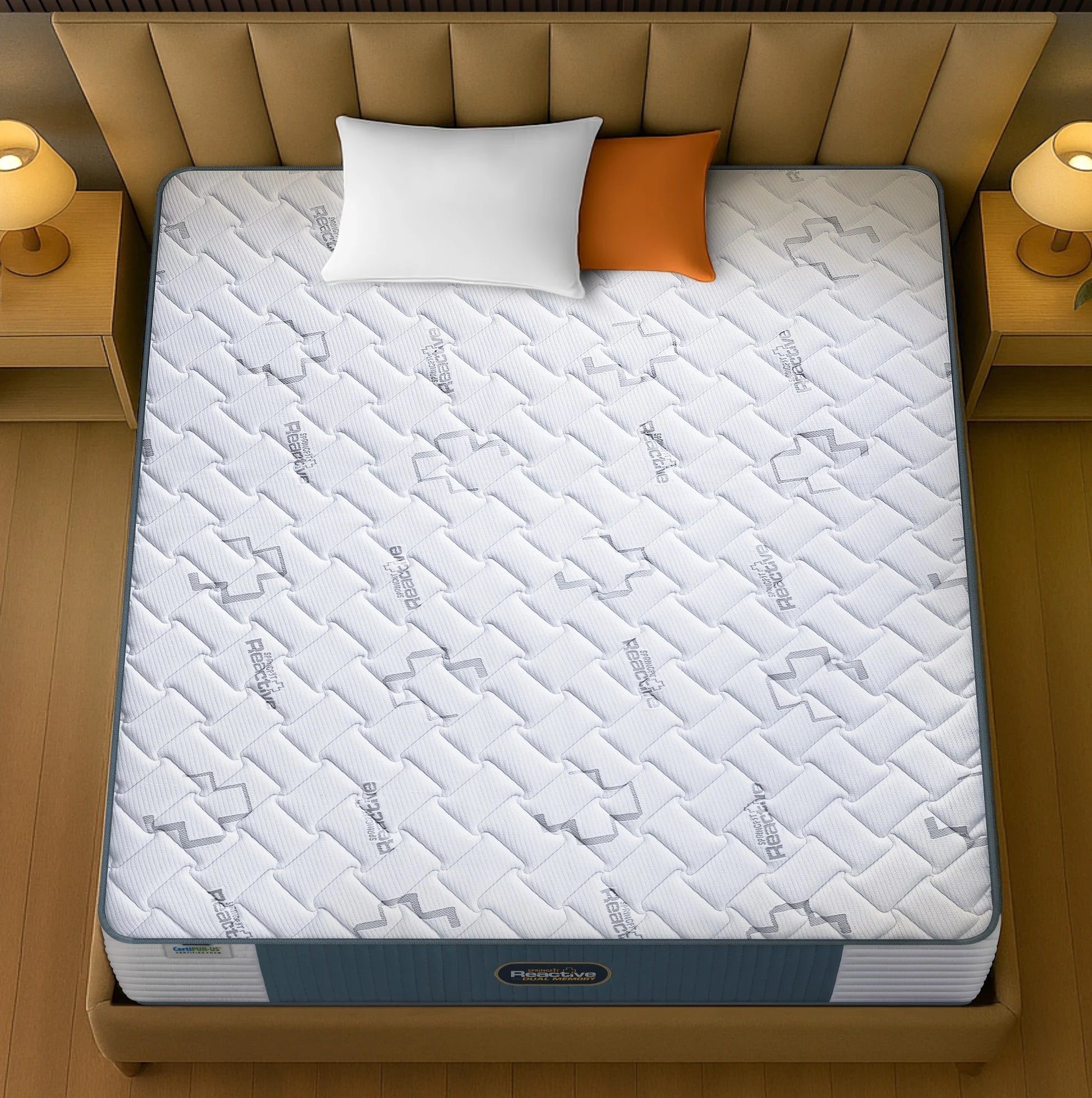 Springfit Reactive Dual Memory mattress aerial top view showing white Health+ branded quilted fabric with logo pattern on beige channeled bed frame with white and orange pillows and warm side lamps