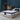 Springfit Reactive Gold mattress lifestyle image with couple in casual outfits — woman seated and man standing — on beige upholstered bed with teal and beige pillows in dramatic dark teal accent bedroom with floor lamp