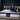 Springfit Reactive Gold mattress lifestyle image with woman in navy blue satin outfit seated on mattress with open magazine on beige platform bed in dark teal bedroom with twin floor lamps and indoor plant