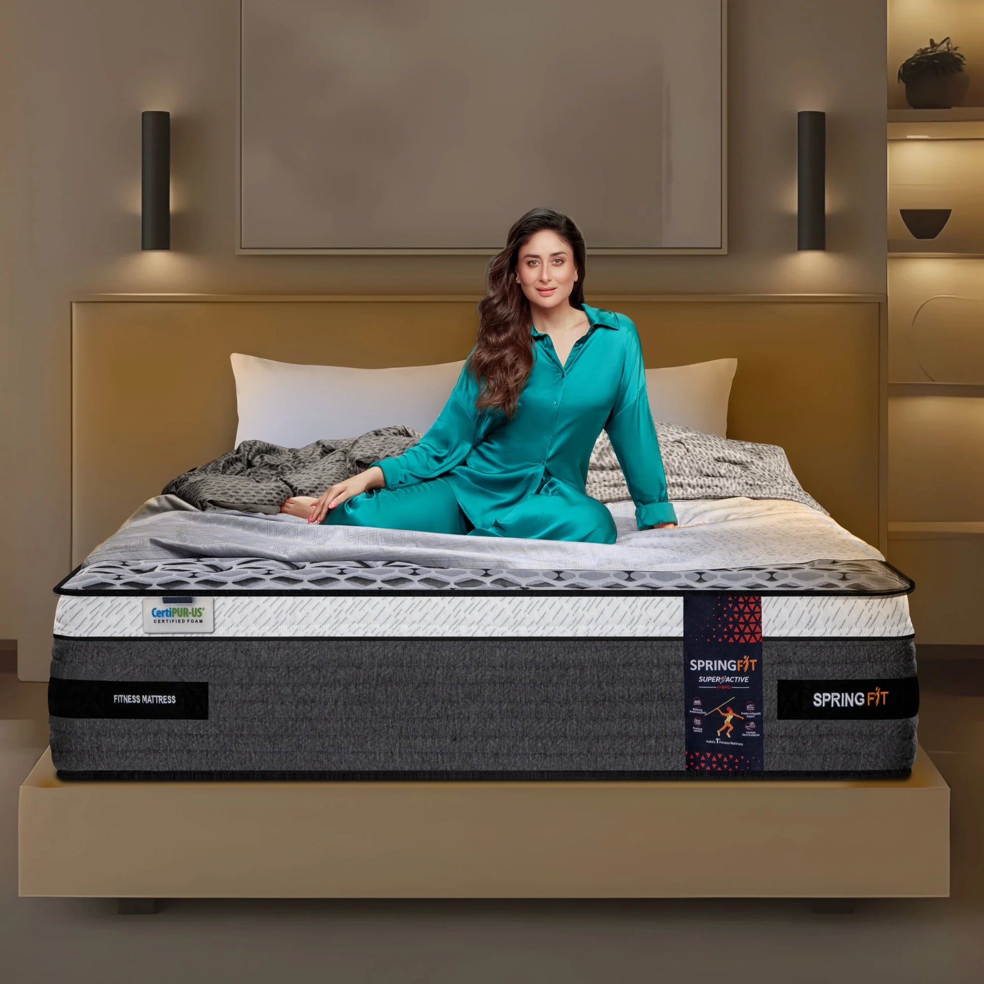 Springfit Super Active Hybrid fitness mattress with CertiPUR-US certification on a beige platform bed with brand ambassador seated in a warm-toned modern bedroom