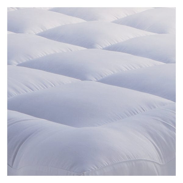 Close-up corner view of Springfit mattress topper showing plush white tufted surface and elastic securing band fitted over a grey herringbone-pattern mattress